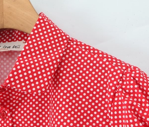 Detail view of the flat collar and puff sleeve design on a red polka dot women shirt