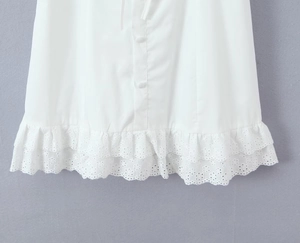 Close-up of white summer dress hem featuring floral embroidery and covered buttons