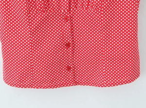 Detailed view of red polka dot blouse with pleated texture and matching red buttons