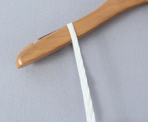 Detailed close-up of white spaghetti strap and texture on a natural wooden hanger