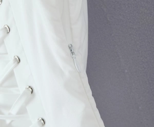 Detail of white dress featuring side hidden zipper and lace-up design with metal eyelets