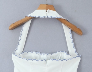 Detail of white halter dress featuring blue scalloped embroidery and hidden back zipper