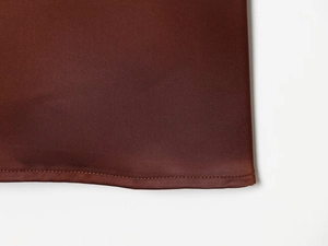 Macro shot of terracotta satin fabric showing twill weave texture and neat rolled hem