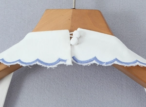 Close-up of white peter pan collar with blue wave embroidery and back cloth buttons