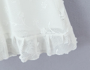 Close-up of white lace dress featuring intricate floral embroidery and ruffled edge details