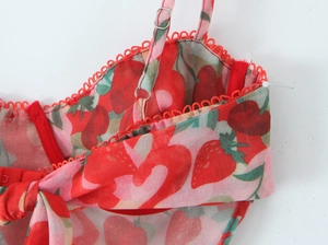 Detail of red strawberry print top with adjustable straps and wavy scallop lace trim