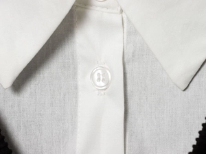 Détail d'un col blanc classique et d'un bouton en résine sur une chemise en popeline