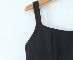 Détail des bretelles de robe noire et décolleté carré sur un cintre en bois