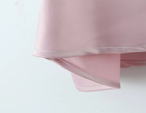 Detailed close-up of pink satin dress hem featuring white contrast stitching and fine fabric