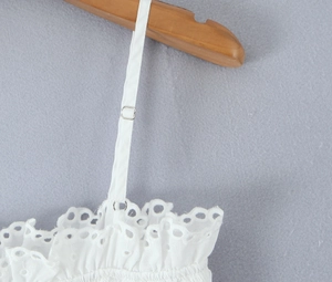 Detail of white eyelet lace embroidery with adjustable shoulder straps and silver buckles