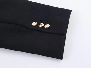 Détail du poignet noir avec trois boutons dorés irréguliers au design moderne de veste