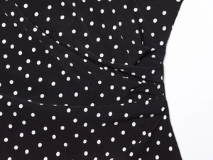 Detail of black polka dot dress featuring elegant wrap design and side pleats texture