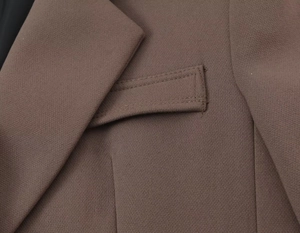 Detail of coffee brown blazer featuring a classic flap pocket and precise stitching texture