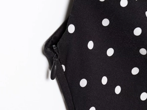 Detail view of the concealed side zipper on a black and white polka dot summer dress