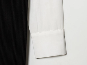 Detail van de zwarte ribstof en witte popeline mouw met een omgeslagen manchetontwerp