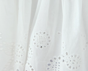 Close-up of white cotton fabric featuring intricate floral Broderie Anglaise eyelet embroidery