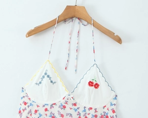 Close-up of floral embroidery detail with cherry patterns and bow on white sundress