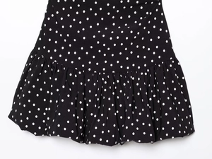 Detailed close-up of a black polka dot mini dress featuring pleated ruffle hem details