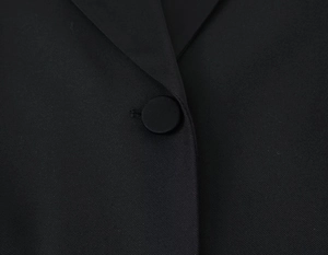 Gros plan sur la texture du blazer noir et son bouton recouvert de tissu assorti