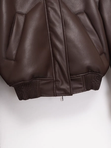 Detailed close-up of dark brown leather jacket with ribbed hem and metal zipper