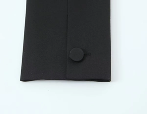 Détail du poignet d'un costume noir montrant la texture du tissu et un bouton recouvert de tissu