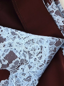 Close-up of intricate light blue floral lace stitching on dark burgundy fabric