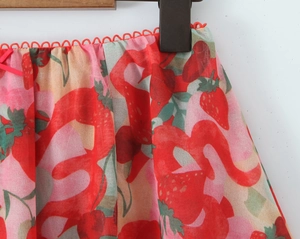 Close-up of strawberry print fabric with red wave lace trim and small bow detail