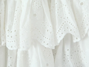 Detailed macro shot of white floral embroidery and scalloped edges on layered cotton fabric