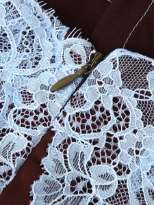 Detailed close-up of delicate white floral lace stitched to dark burgundy fabric with hidden zipper