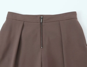 Close-up of coffee brown suit pants featuring metal zipper closure and pleated texture