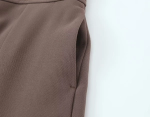 Detailed view of the side pocket stitching and woven texture of dark brown trousers