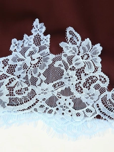 Detail of light blue floral lace fabric with delicate eyelash trim and intricate texture