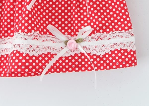 Detailed close-up of red polka dot dress fabric with lace trim and pink floral bow