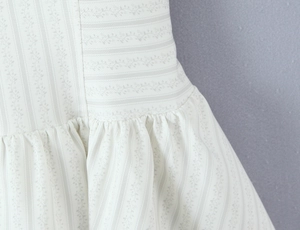Détail de l'imprimé floral et des plis sur une robe d'été crème à fines bretelles