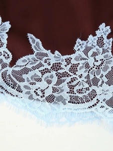 Detailed close-up of blue floral lace trim with eyelash edges on burgundy fabric
