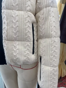 Detail of cable-knit texture and black metal zippers on a creamy white winter jacket