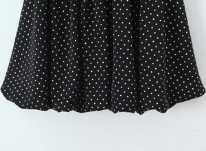 Detail shot of black woven fabric with classic white polka dot pattern and smooth hem