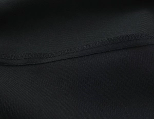 Gros plan détaillé montrant les coutures surjetées sur le tissu tissé noir du costume