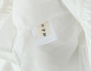 Close-up of woven brand label with size S and satin care tag on white embroidered top