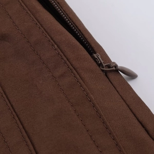Macro shot of durable metal zipper and refined parallel stitching on brown pleated fabric