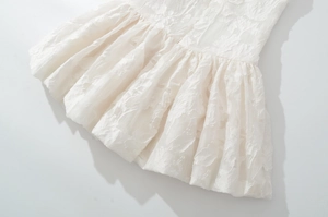Détail de la robe blanche avec broderie florale 3D et texture plissée sur le bas