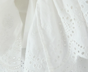 Detailed view of white eyelet embroidery and scalloped lace on summer cotton fabric