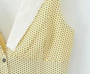 Close-up of yellow polka dot dress featuring white lace trim and black button details
