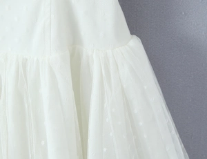Close-up of white Swiss dot mesh fabric with layered ruffles and pleated details