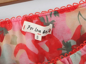 Detailed close-up of strawberry print fabric and red crochet lace neckline trim