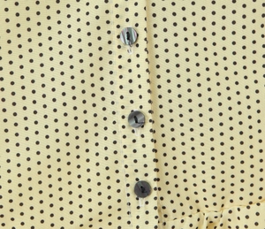Close-up of yellow polka dot fabric with iridescent mother-of-pearl buttons and topstitching