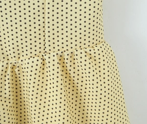 Close-up of yellow polka dot fabric detailing fine pleats and stitching on the dress