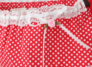 Close-up of red polka dot fabric featuring white lace trim and pink ribbon rose detail