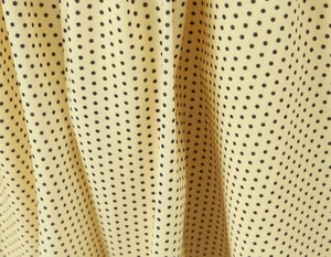 Close-up of yellow chiffon dress fabric with classic black polka dot pattern and soft draping