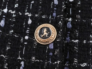 Close-up of metallic lion crest button on premium black tweed blazer fabric with silver threads